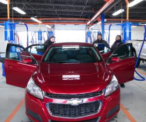 Three car technicians cleaning a red sedan with a Eurovac detailing system